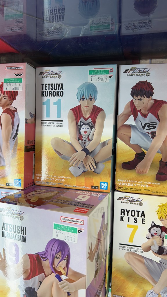 Akihabara'da bir mağaza rafında Kuroko's Basketball anime figür kutuları ve 3000 Yen fiyat etiketleri.